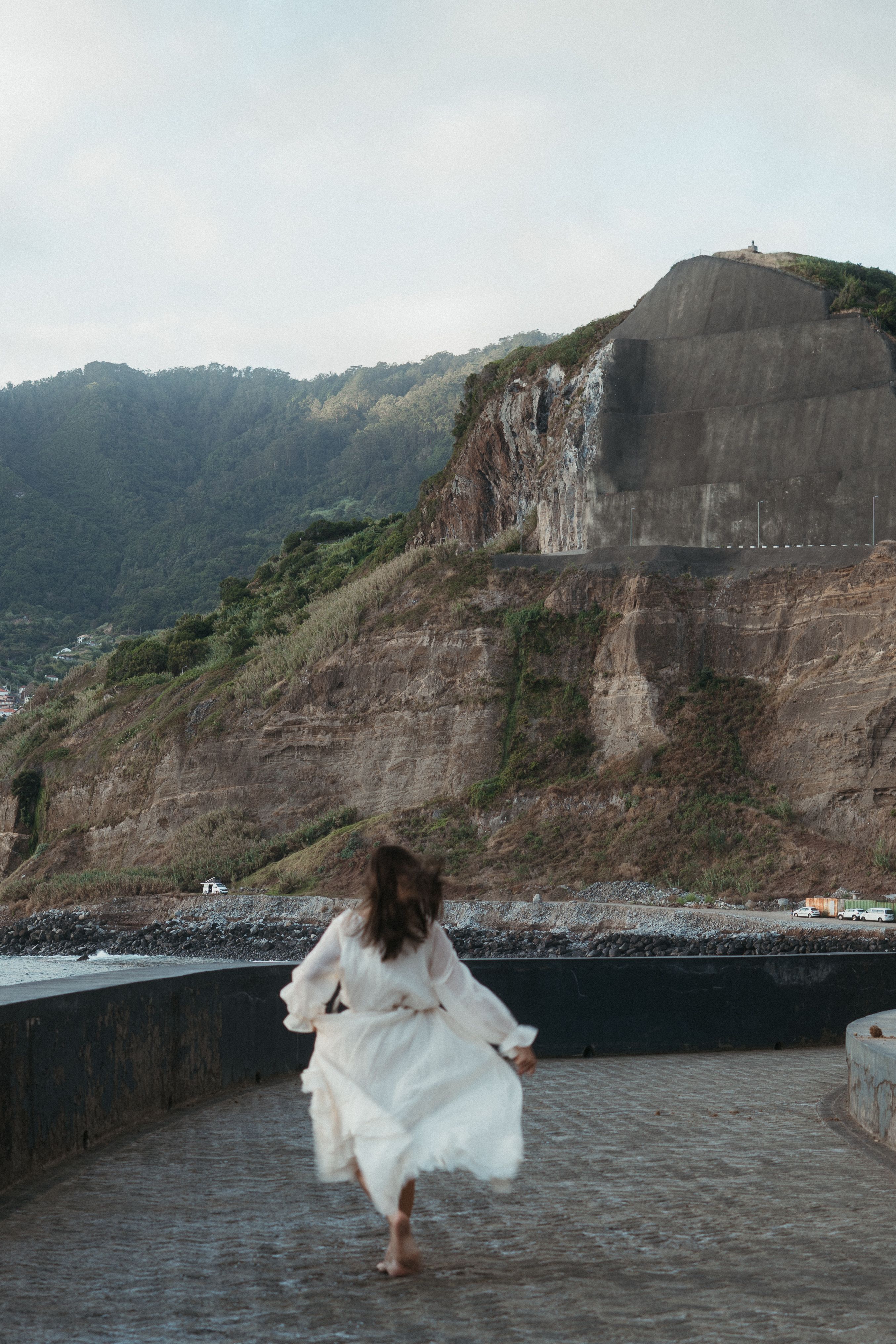 Woman in a white dress running along a road by the cliffs