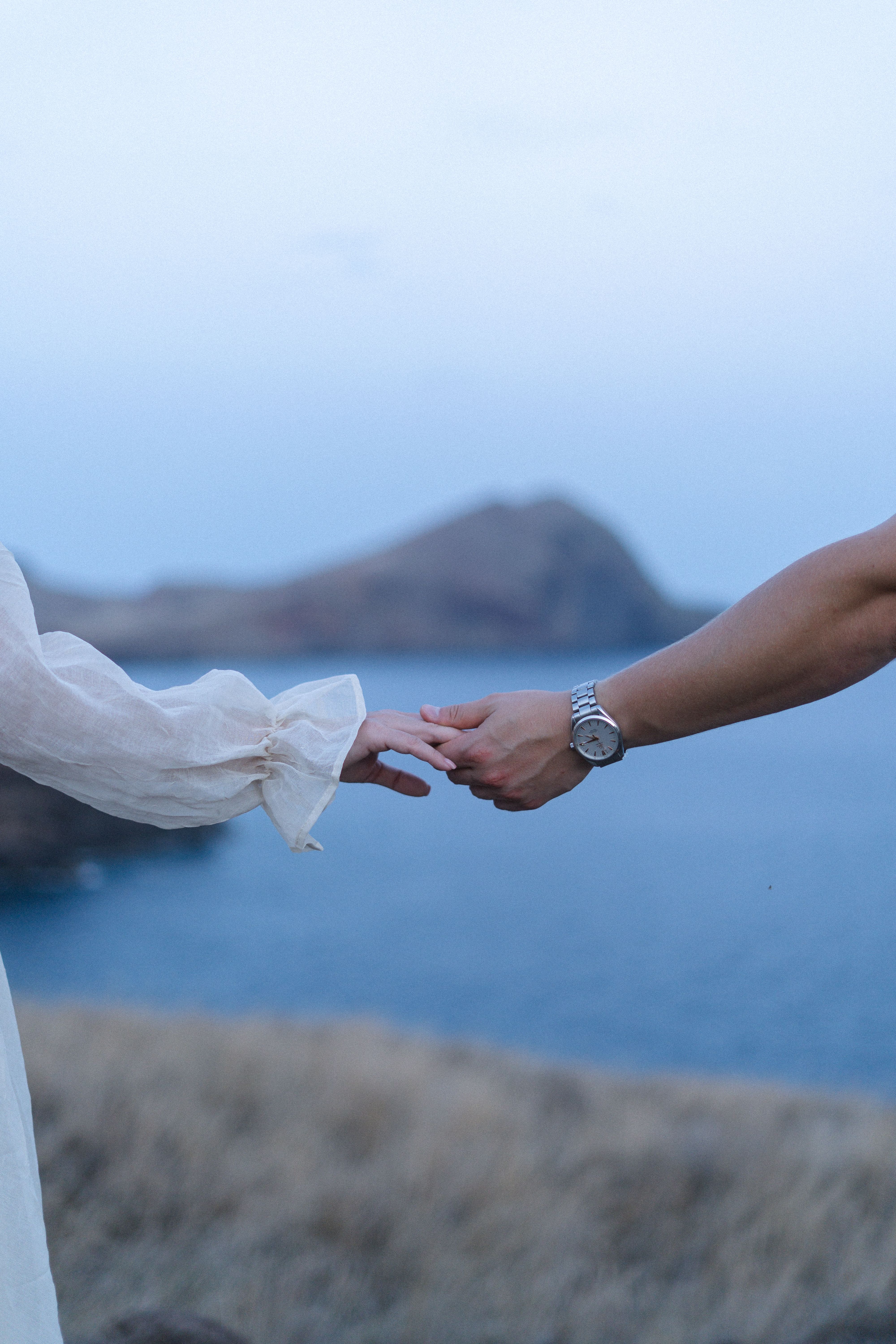 Couple's hands touching against the ocean